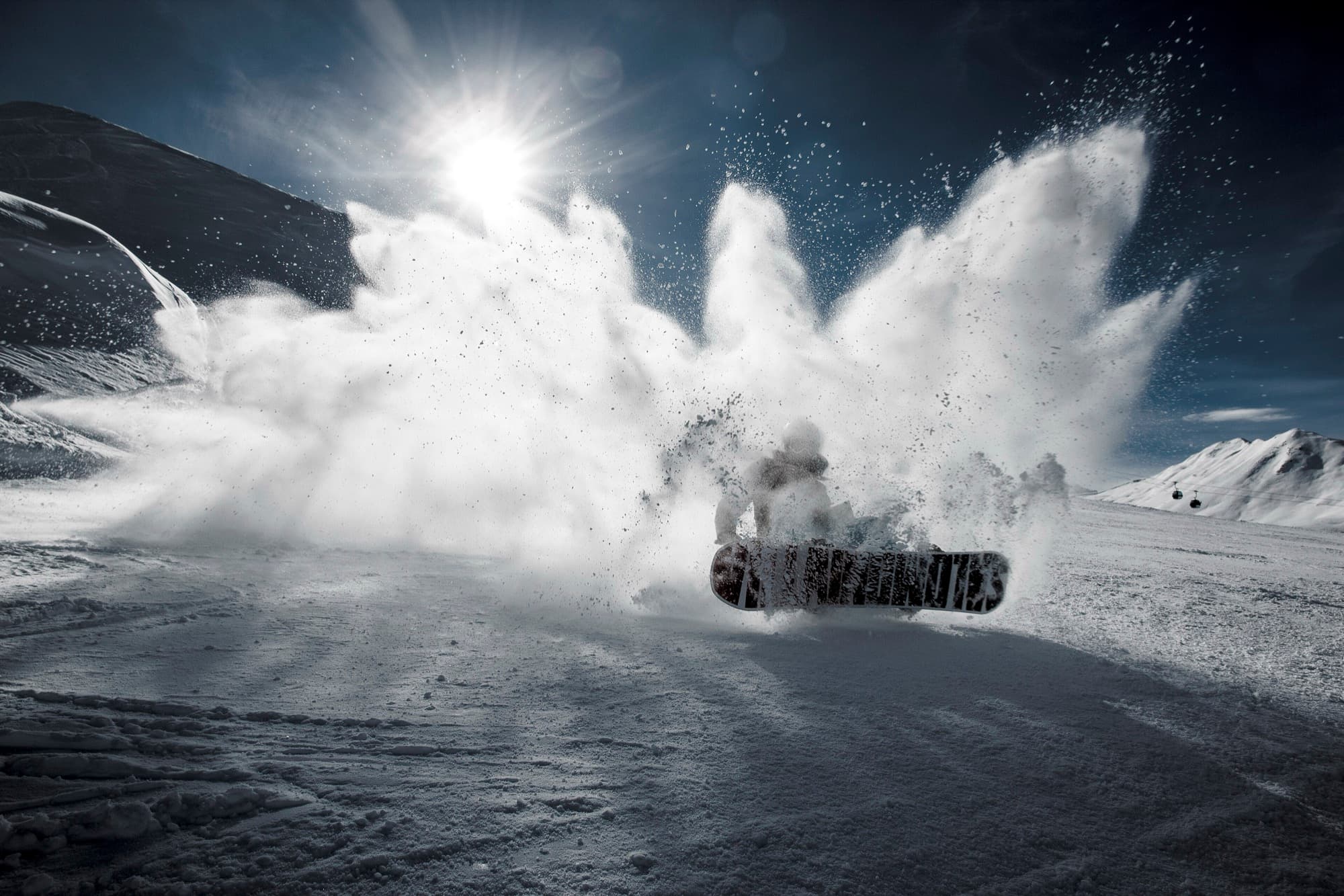 Snowboarder throwing up a wall of powder, pine and sunflower duotone